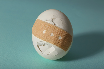Cracked egg wrapped in court plaster on turquoise background